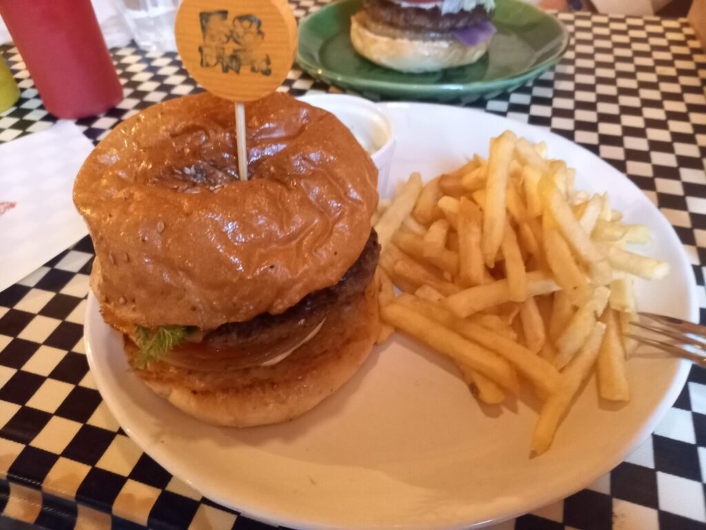 串に刺された大きなハンバーガーとセットのフライ、奥には、コールスローA large burger on a skewer with a set of fries; in the back, coleslaw